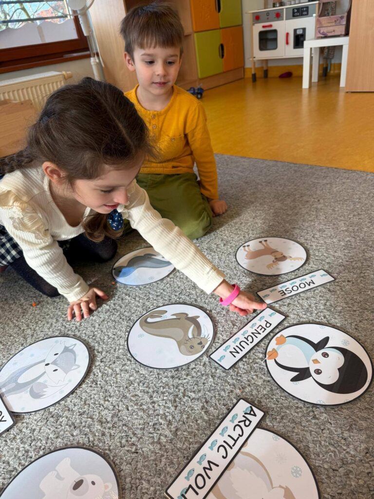 Dwoje dzieci bawiących się z kartami przedstawiającymi zimowe zwierzęta na podłodze.